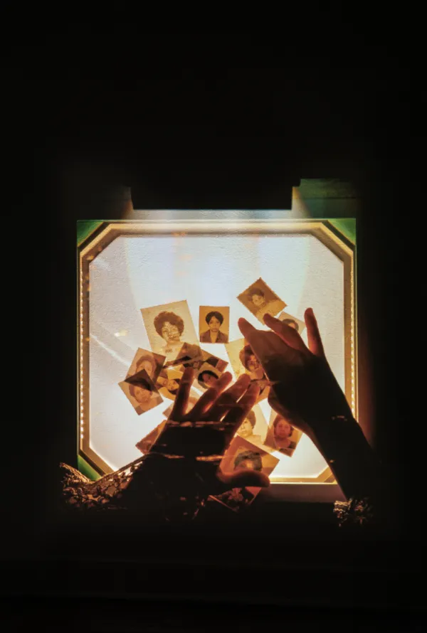 A photo of a transparency overhead projector seeing from the top, in a dark space. In the surface, with yellow greenish colours, one can see two hands and some ID-photos of a woman.